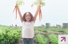 Young African American girl holding carrots outside in a garden. 