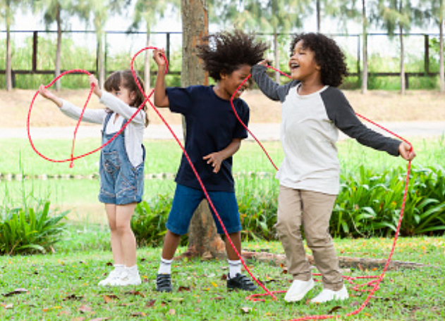Three diverse children jump-roping outside. 