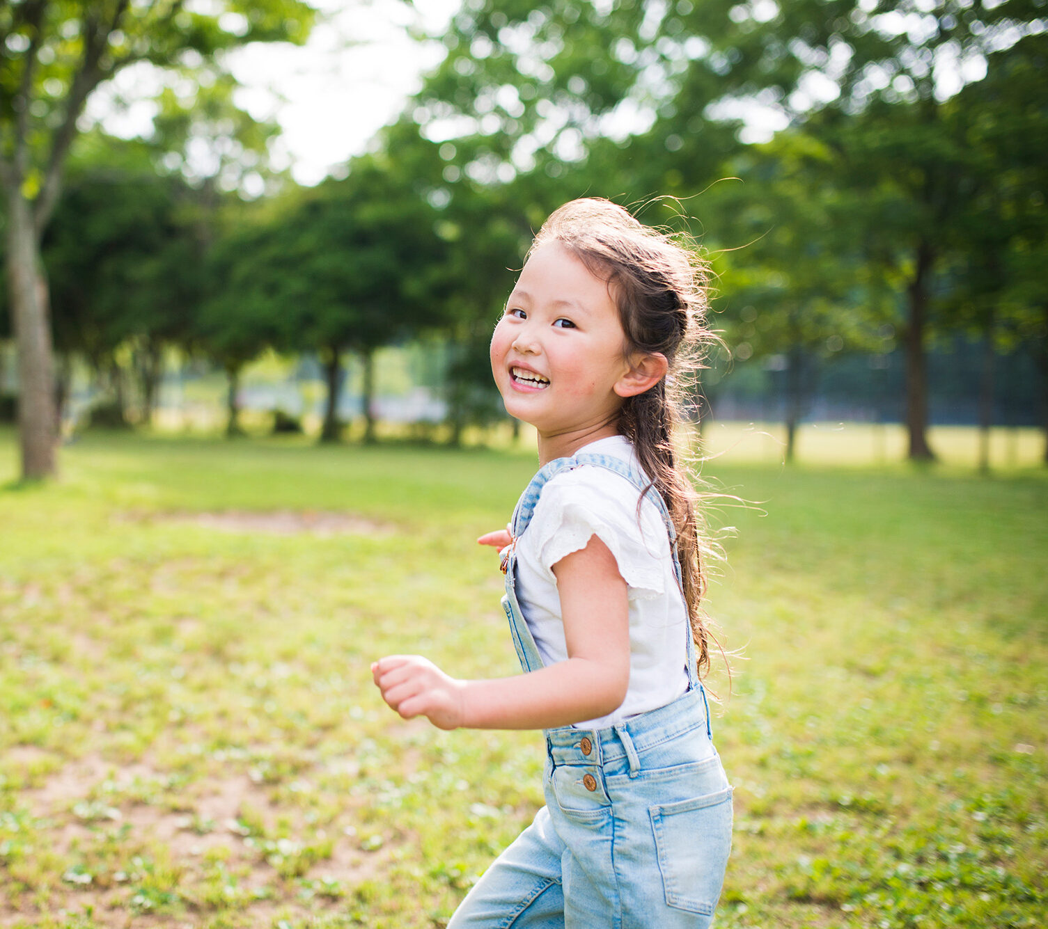 Young Asian girl playing outside smiling and running.