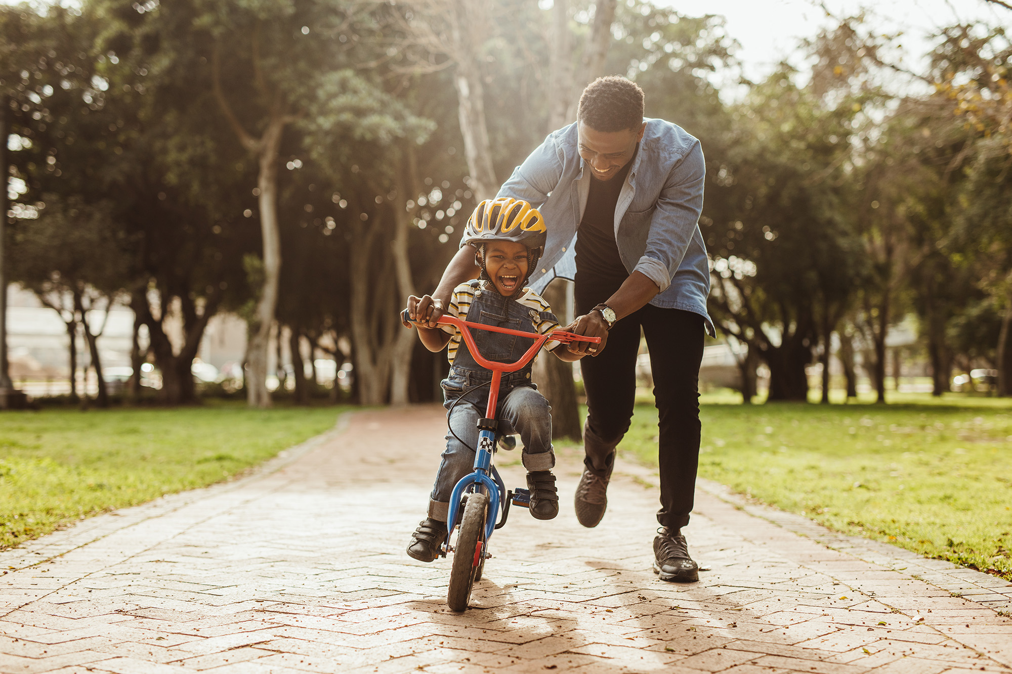 Young African American boy with helmet on learning to ride his bike with his father.